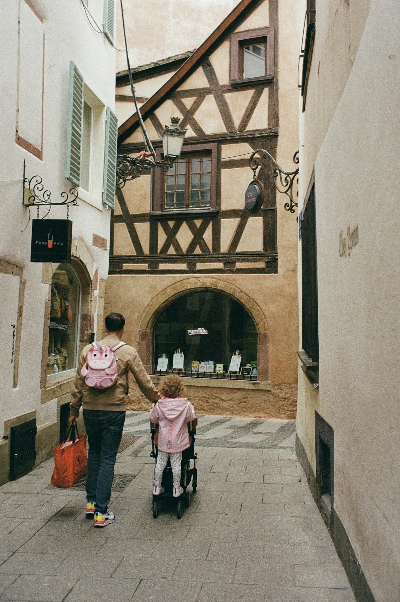 A father and daughter walk through the picturesque streets of Strasbourg, showcasing traditional architecture.