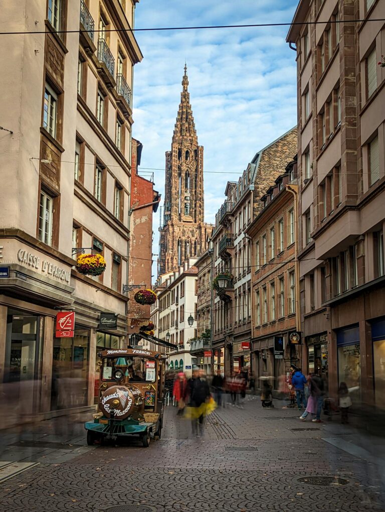 A lively street scene in Strasbourg showcasing the iconic Notre-Dame Cathedral in the background.